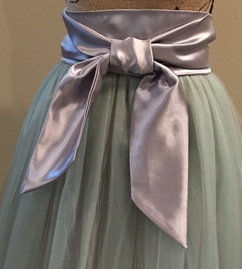 May include: A light green tulle skirt with a wide silver satin sash tied in a bow at the front.