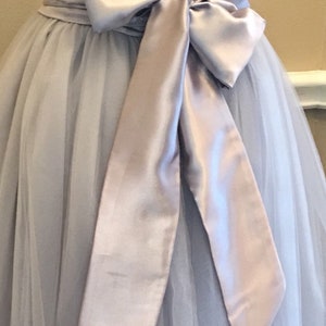 May include: A light gray tulle skirt with a matching satin sash tied in a bow at the back.