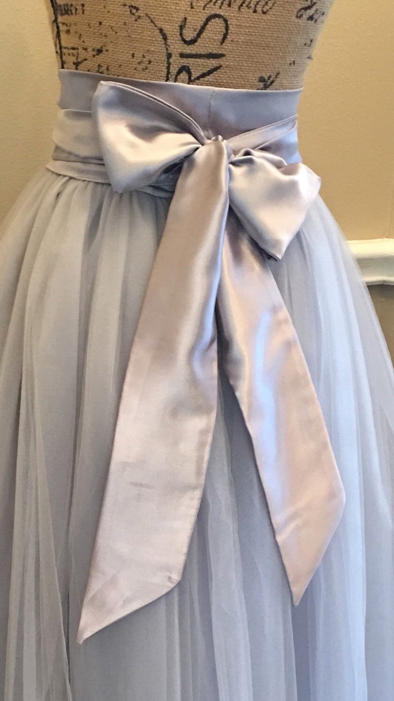 May include: A light gray tulle skirt with a matching satin sash tied in a bow at the back.