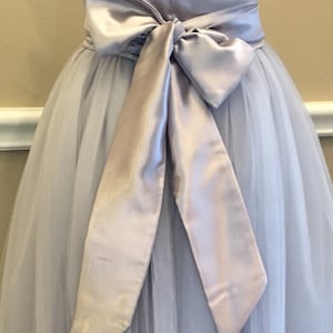 May include: A light gray tulle skirt with a wide silver satin sash tied in a bow at the waist.