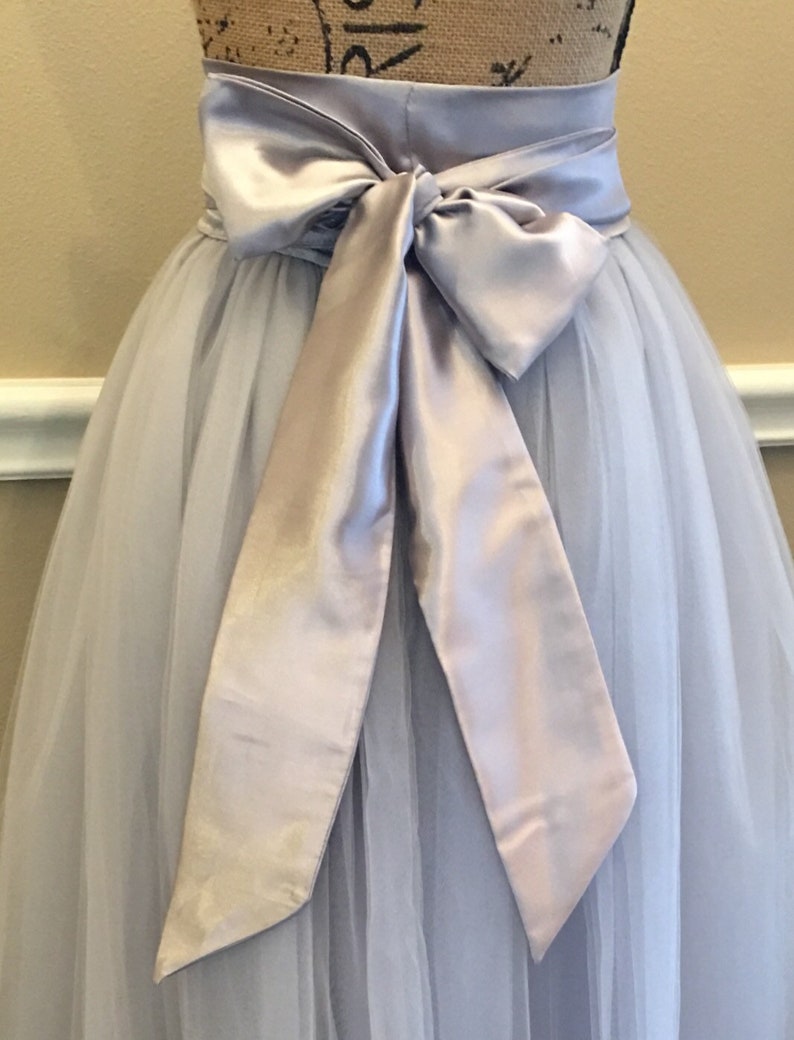 May include: A light gray tulle skirt with a wide silver satin sash tied in a bow at the waist.