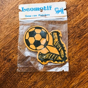 May include: A package of two sew-on patches featuring a black and white soccer ball and a black and white soccer cleat. The patches are on a yellow background and the package says "Leomotif Sew-on Patches".