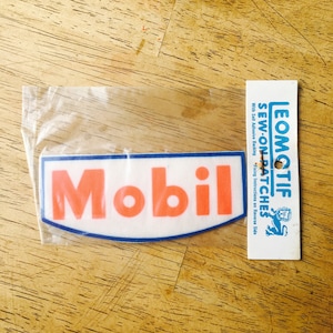 May include: A white sew-on patch with blue trim and the word "Mobil" in orange letters. The patch is packaged in a clear plastic bag with a white card that says "LEOMOTIF SEW-ON PATCHES With Self Adhesive Backing. Full Instructions on Reverse Side."
