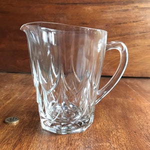 May include: A clear glass jug with a diamond pattern. The jug has a wide mouth and a handle.