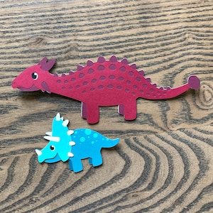 May include: Two paper cutouts of dinosaurs. A red dinosaur with a spiky back and a blue dinosaur with three horns on its head.