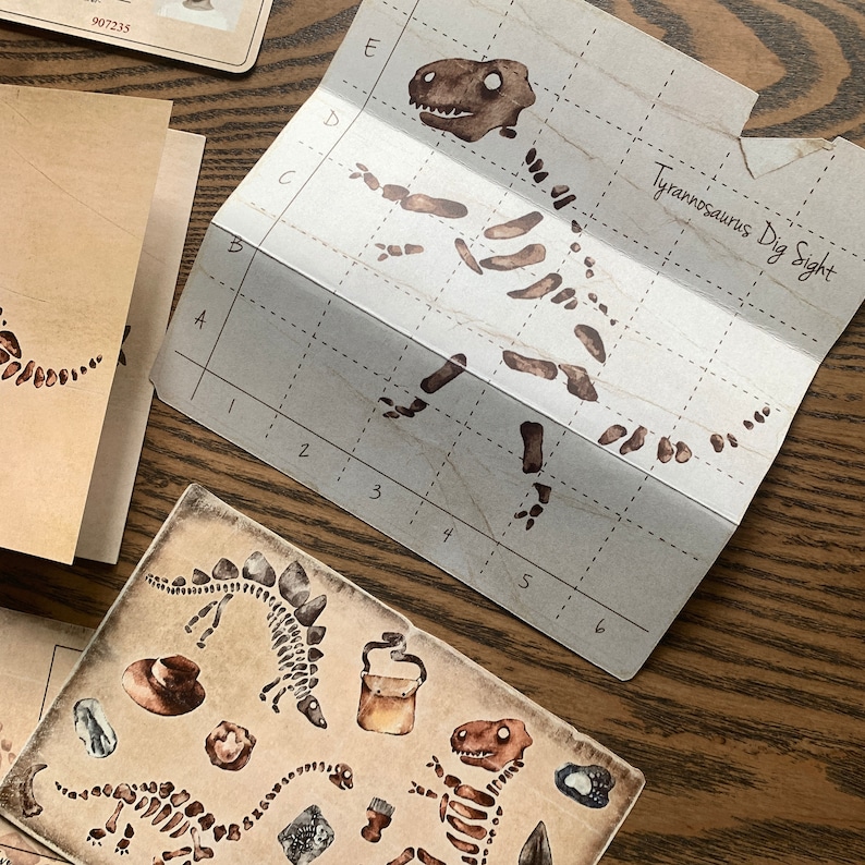 May include: A brown and white paper game board with a grid and the text "Tyrannosaurus Dig Sight". The game board is folded in half and shows a brown and white dinosaur skeleton.