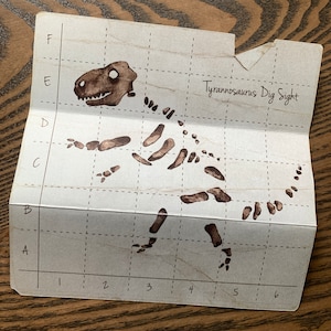 May include: A black and white illustration of a Tyrannosaurus Rex skeleton on a gridded paper background. The text "Tyrannosaurus Dig Sight" is written in the top right corner.