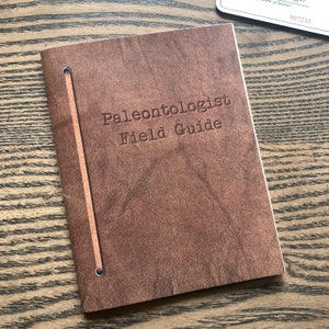 May include: A brown leather-bound field guide with the title "Paleontologist Field Guide" embossed on the front cover.