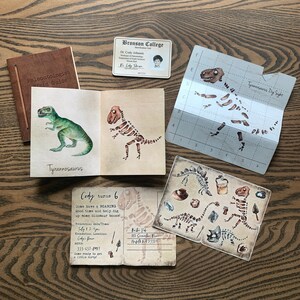 May include: A paleontologist field guide with a Tyrannosaurus Rex skeleton illustration. A birthday invitation for Cody's 6th birthday party with a dinosaur dig theme. The invitation includes a date, time, and location for the event. The invitation also includes a RSVP number and a message to come ready to get a little dirty.