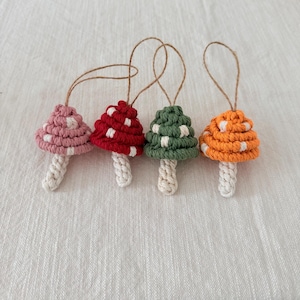 May include: Four handmade mushroom ornaments in pink, red, green, and orange with white polka dots. Each mushroom has a white stem and a natural twine loop for hanging. These decorative ornaments are perfect for adding a touch of whimsy to any space.