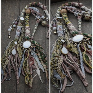 Peut inclure: Un accessoire de coiffure décoratif composé de bandes de tissu tressées dans des tons de vert, marron et crème. Il comprend un pendentif central en pierre blanche, des breloques en pierre en forme de goutte, des perles en bois et en verre.