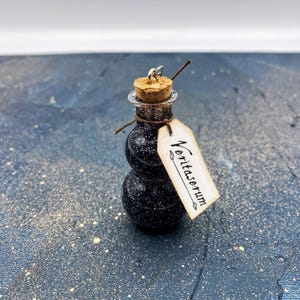May include: A small glass bottle with a cork stopper and a black glitter-like liquid inside. The bottle has a tag attached to it that says "Veritaserum".