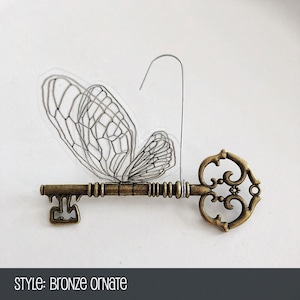May include: A bronze ornate key with a delicate butterfly design attached to the bow. The butterfly is made of clear plastic with a wire loop.