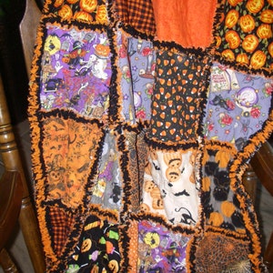 May include: A handmade Halloween quilt featuring a variety of orange, black and purple fabric squares. The quilt incorporates a range of Halloween themes, including pumpkins, bats, ghosts and candy corn. The quilt is finished with a frayed edge and is ideal for adding a spooky touch to your home decor.