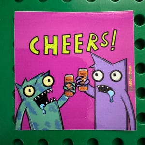 May include: A square sticker with a magenta background features two cartoon monsters toasting beer cans. The word "CHEERS!" is written in large, yellow, block letters. The sticker has the artist's signature in the bottom right corner.