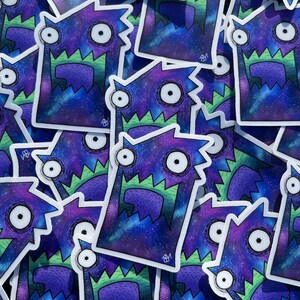 May include: A collection of stickers featuring a cartoon monster design. The monster has a purple and blue galaxy-like body, green jagged teeth, and large white eyes. The stickers are scattered on a black surface.