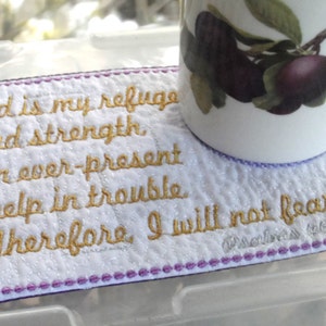 May include: A white fabric coaster with purple stitching and a gold embroidered quote: "God is my refuge and strength, an ever-present help in trouble. Therefore, I will not fear..."  The quote is from Psalms 46:7-3.
