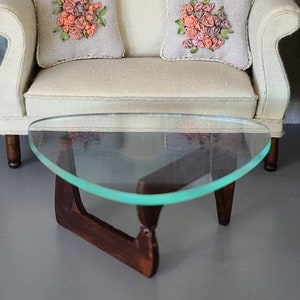 May include: A white fabric sofa with two pillows featuring embroidered floral designs in shades of pink and brown. A glass top coffee table with a dark wood base sits in front of the sofa.