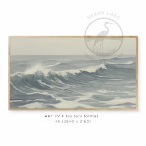 Op de afbeelding: Een ingelijste prent van een zeegezicht met een brekende golf in grijstinten en blauwtinten. Het rechthoekige kunstwerk heeft een licht houten frame. De prent is voorzien van het label "HERON LAKE PRINTS & GRAPHICS".