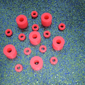 May include: Assortment of red plastic rings of varying sizes. The rings are arranged on a blue and green glittery surface.