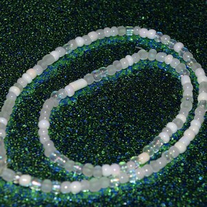 May include: A white and iridescent beaded necklace with a green background.