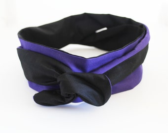 May include: A reversible headband featuring a black and purple design. The headband is knotted at the front, with the black fabric visible on one side and purple on the other. The accessory is made of soft fabric.