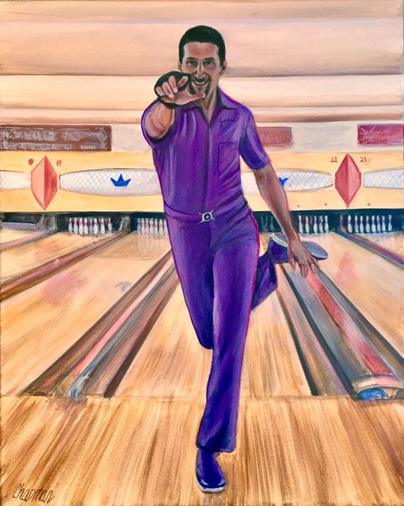 Jesus Quintana wearing his purple bowling suit with purple shoes is pointing with his right hand and one leg kicked up behind him. He has a big smile on his face after he bowled a strike. classic bowling alley behind him with pins and lanes.