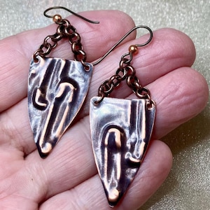 May include: A pair of silver and copper earrings with a hammered texture and a chain link design. The earrings are shaped like a teardrop and have a small loop at the top for attaching to an earring hook.