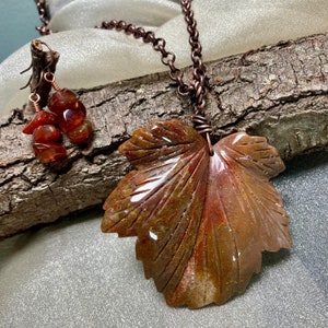 May include: A copper necklace with a carved agate leaf pendant and matching earrings. The agate is a mix of brown, red, and white colors.