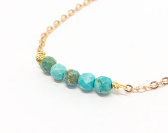 May include: A gold chain necklace with a row of turquoise blue beads.