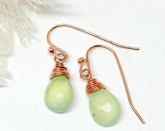 Puede incluir: Un par de aretes delicados con piedras preciosas de color verde claro en forma de lágrima envueltas en alambre de cobre. Los aretes tienen un diseño simple y elegante y son perfectos para el uso diario.