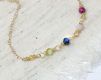 May include: A gold chain necklace with five gemstone beads. The beads are yellow, green, blue, pink, and red.