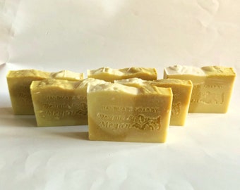 May include: Five rectangular bars of yellow soap with a white top layer. Each bar is embossed with the text 'HANDMADE SOAP BY Designs By Megan' on the front face. The soap bars are arranged in a staggered formation against a plain white background.