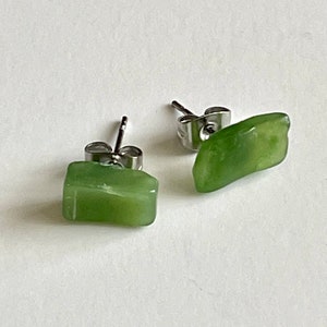 May include: A pair of silver stud earrings with green jade stone accents. The stones are irregularly shaped and have a natural, polished finish.