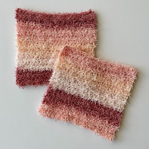 Puede incluir: Dos paños de cocina de ganchillo en un degradado de rosa, melocotón y blanco. Los paños de cocina están hechos con un hilo esponjoso y tienen una superficie texturizada.