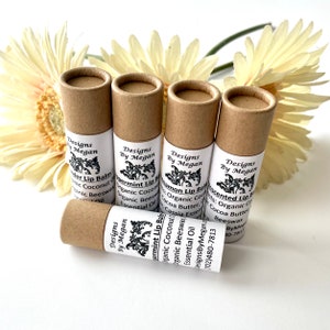 May include: Five brown cardboard tubes with white labels containing lip balm. The labels have black text that reads "Designs By Megan" and the flavor of the lip balm. The flavors are "Peppermint Lip Balm", "Cinnamon Lip Balm", "Unscented Lip Balm", and "Lavender Lip Balm".