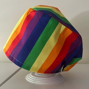 May include: A rainbow striped fabric scrub hat with a drawstring tie. The hat is made of cotton and is designed to be worn by medical professionals.