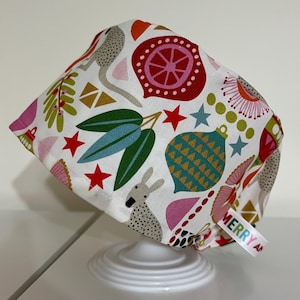 May include: A white surgical scrub cap with a colorful pattern of red stars, green leaves, and teal ornaments. The cap features a repeating design with a kangaroo and the text "MERRY AN".
