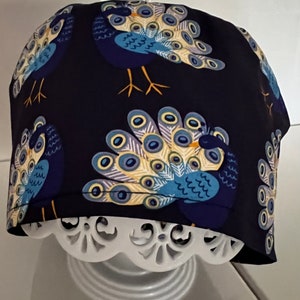 May include: A dark blue scrub hat with a peacock print. The peacocks are in shades of blue, yellow, and white.