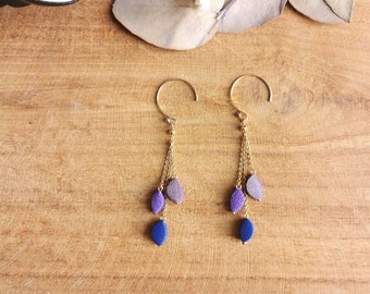 May include: A pair of gold dangle earrings with three purple and blue teardrop-shaped beads hanging from each earring.