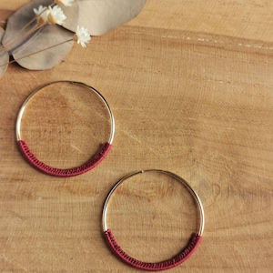 May include: Two gold hoop earrings with a burgundy cord wrapped around half of each hoop.