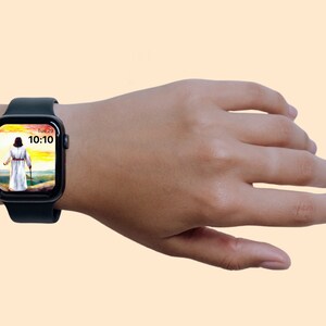 May include: A black smartwatch showing a person in white robes walking with a staff against a landscape. The watch face displays the time as 10:10 and the day as Tue 23. The watch is on a wrist against a light orange background.