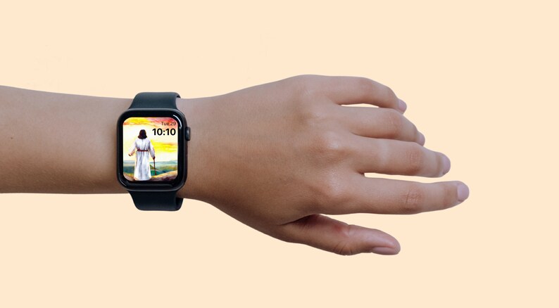 May include: A black smartwatch showing a person in white robes walking with a staff against a landscape. The watch face displays the time as 10:10 and the day as Tue 23. The watch is on a wrist against a light orange background.