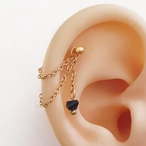 Orecchino a catena con cristalli neri per piercing all'elice e alla conca, realizzato in acciaio inossidabile placcato oro. Orecchino a catena con cristalli neri per piercing a 2 fori o ad anello.