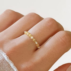 May include: A gold ring featuring a floral pattern and tiny pearls. The ring is worn on a finger. The design includes a repeating pattern of small flowers and pearls. The ring is a delicate piece of jewellery, suitable for everyday wear.