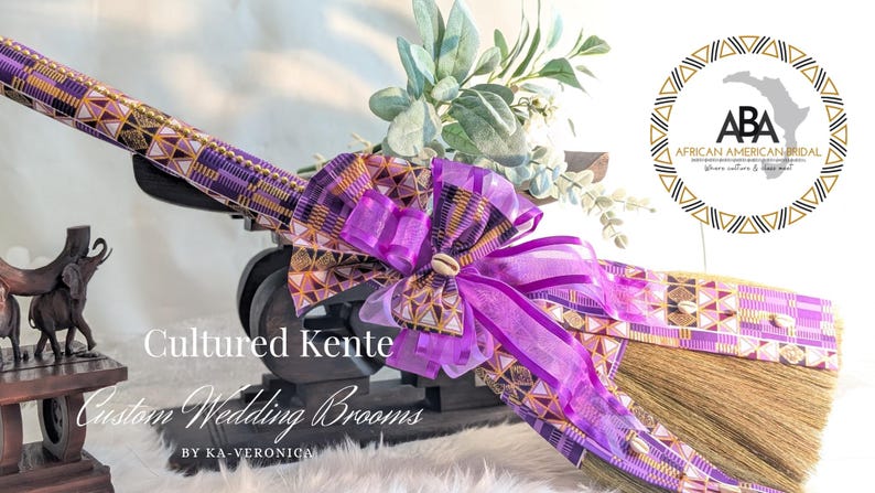 Handcrafted cultured Kente wedding broom by African American Bridal, featuring vibrant multicolor purple and gold  Kente cloth, cowrie shell accents, gold bead detailing, and purple organza bow, designed to honor the African American wedding tradition of jumping the broom.
