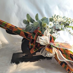 Close-up of a cultured Kente wedding broom by African American Bridal showcasing traditional Kente fabric, symbolic cowrie shells, gold bead accents, and a sheer ivory bow used for Jumping the Broom ceremonies