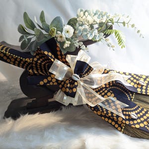 Handcrafted cultured Kente wedding broom by African American Bridal, featuring vibrant multicolor Kente cloth, cowrie shell accents, gold bead detailing, and an ivory organza bow, designed to honor the African American wedding tradition of jumping the broom. Ethnic Fabics available Black & Gold cultured bling Wedding Broom 🧹