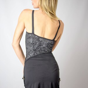 May include: A black mini dress with thin straps. The bodice features a gray floral pattern, and the skirt has a ruffled hem. Gold-colored accents are visible on the side. The dress is made of a soft, flowing fabric.