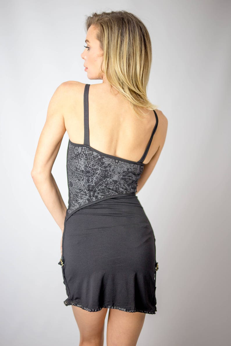 May include: A black mini dress with thin straps. The bodice features a gray floral pattern, and the skirt has a ruffled hem. Gold-colored accents are visible on the side. The dress is made of a soft, flowing fabric.